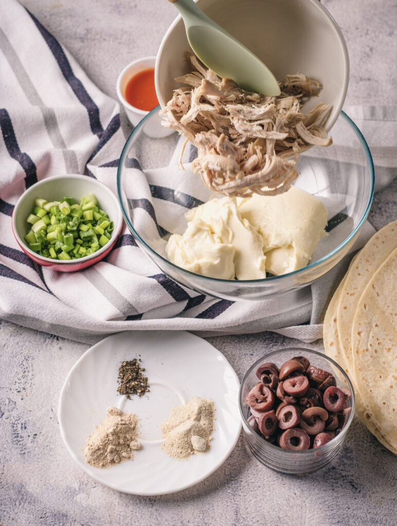 A picture of shredded chicken being dumped into a bowl with softened cream cheese.