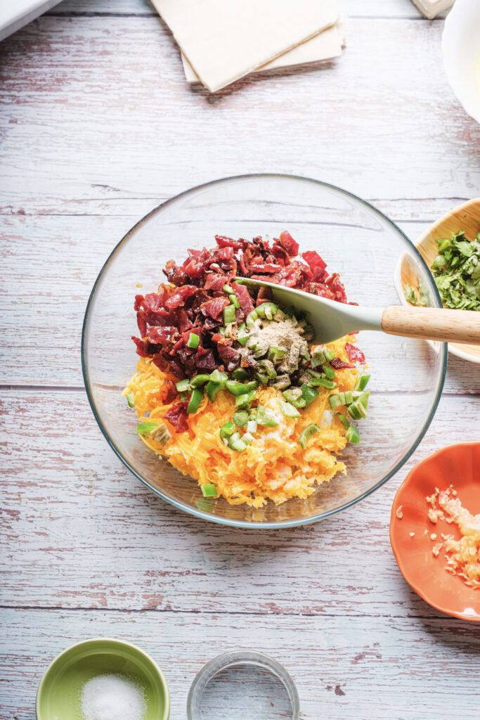 A picture of cream cheese, shredded cheddar, bacon, jalapeño, and spices together in a bowl unmixed.