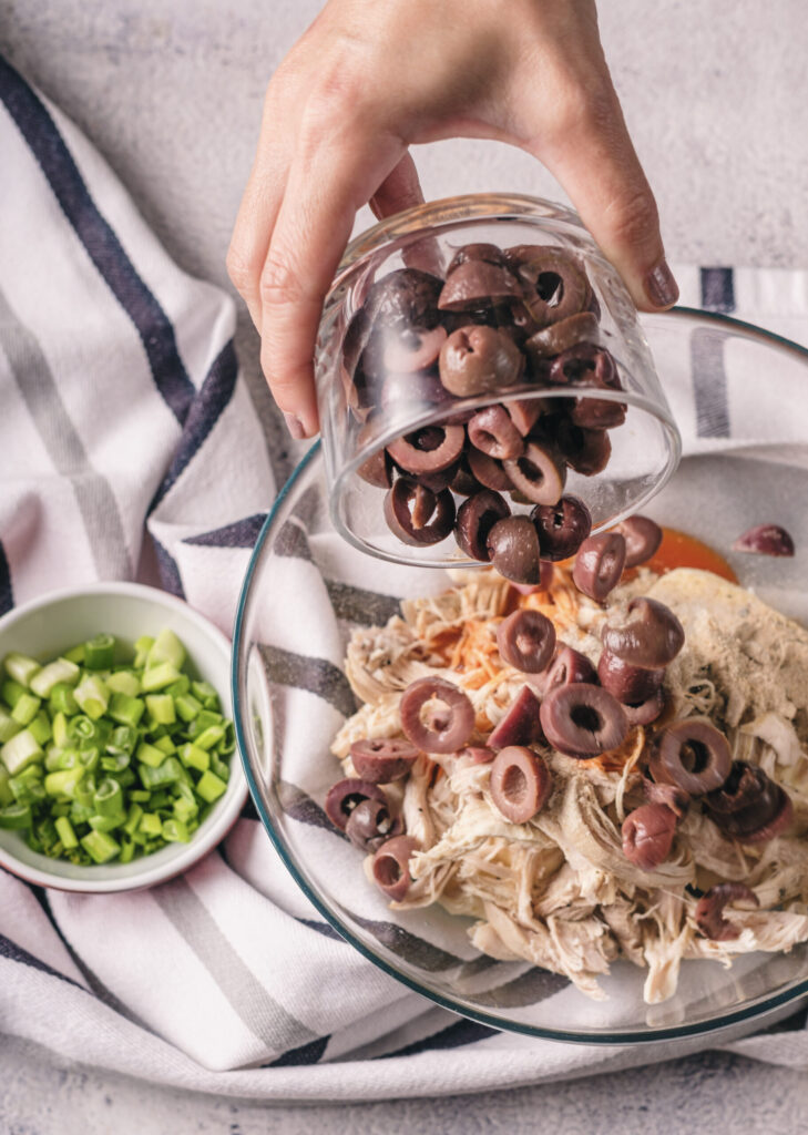A picture of sliced olives being poured into a bowl with a chicken and cream cheese mixture.