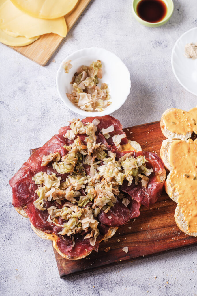 A picture of dinner rolls cut in half, topped with thousand island dressing, pastrami, and sauerkraut.