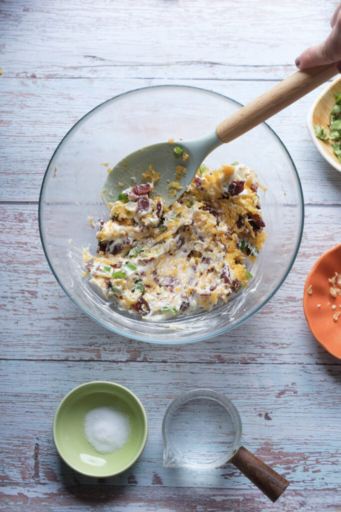 A picture of cream cheese, shredded cheddar, bacon, jalapeño, and spices mixed together in a bowl.