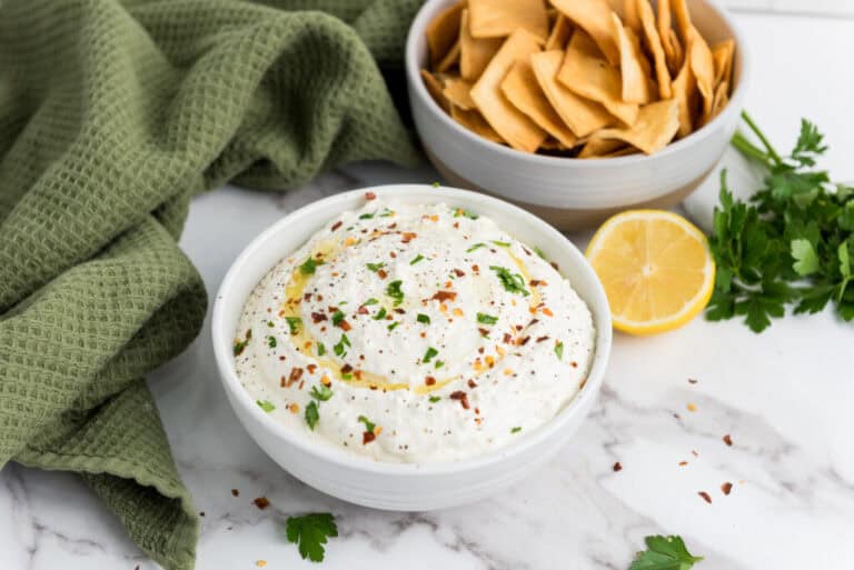 A picture of a bowl of whipped feta dip flanked by chips and a lemon slice.