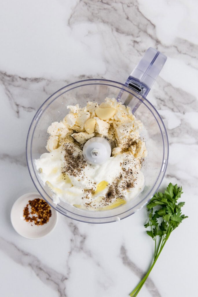 A picture of feta cheese, yogurt, garlic, olive oil, salt, and pepper in a food processor, unblended.