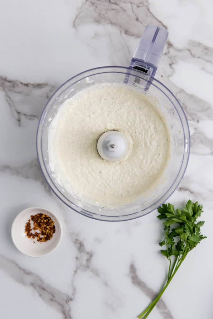 A picture of feta cheese, yogurt, garlic, olive oil, salt, and pepper blended together in a food processor.