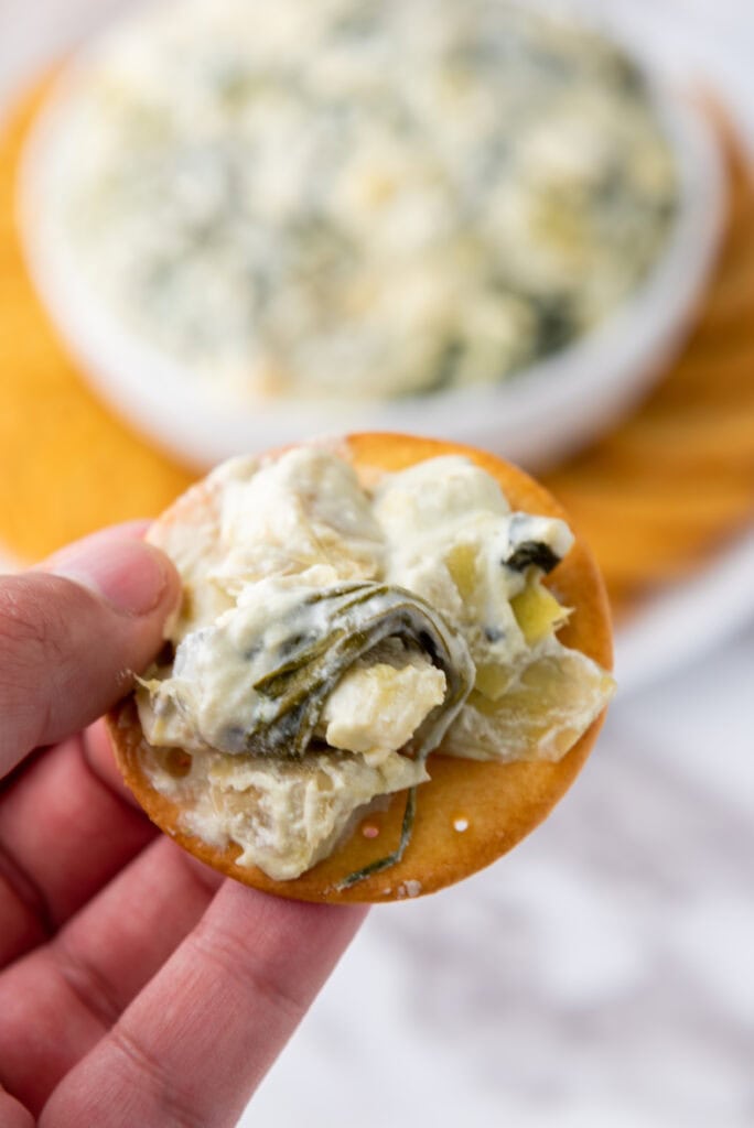 A picture of spinach artichoke dip scooped onto a cracker.