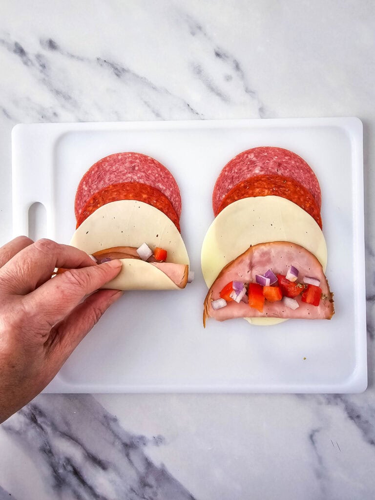 A picture of someone rolling the meat and cheese together like a burrito.