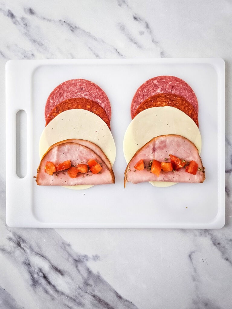 A picture of Italian meats and cheese with tomatoes on the meat.