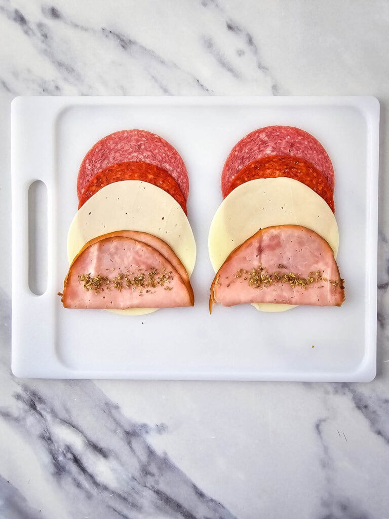 A picture of two rows of Italian meats and cheese with oregano sprinkled onto the meat.