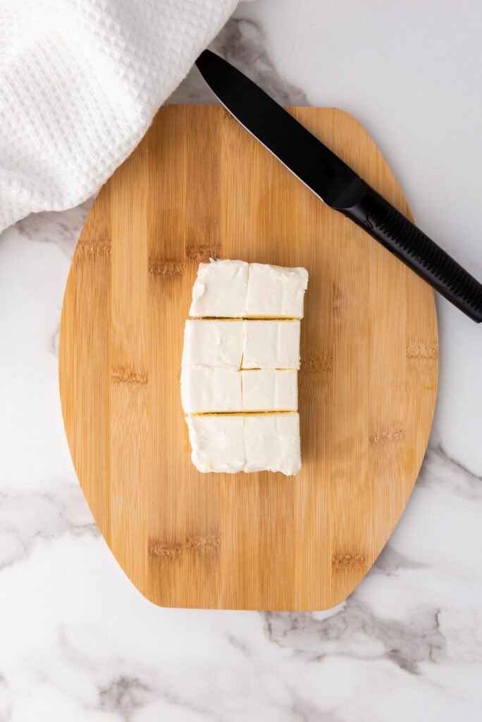 A picture of cream cheese cut into pieces on a cutting board.