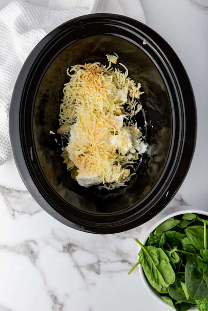 A picture of cream cheese, artichokes, sour cream, and mozzarella cheese in a slow cooker.