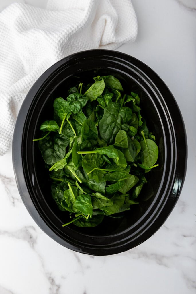 A picture of a large pile of spinach in a slow cooker.