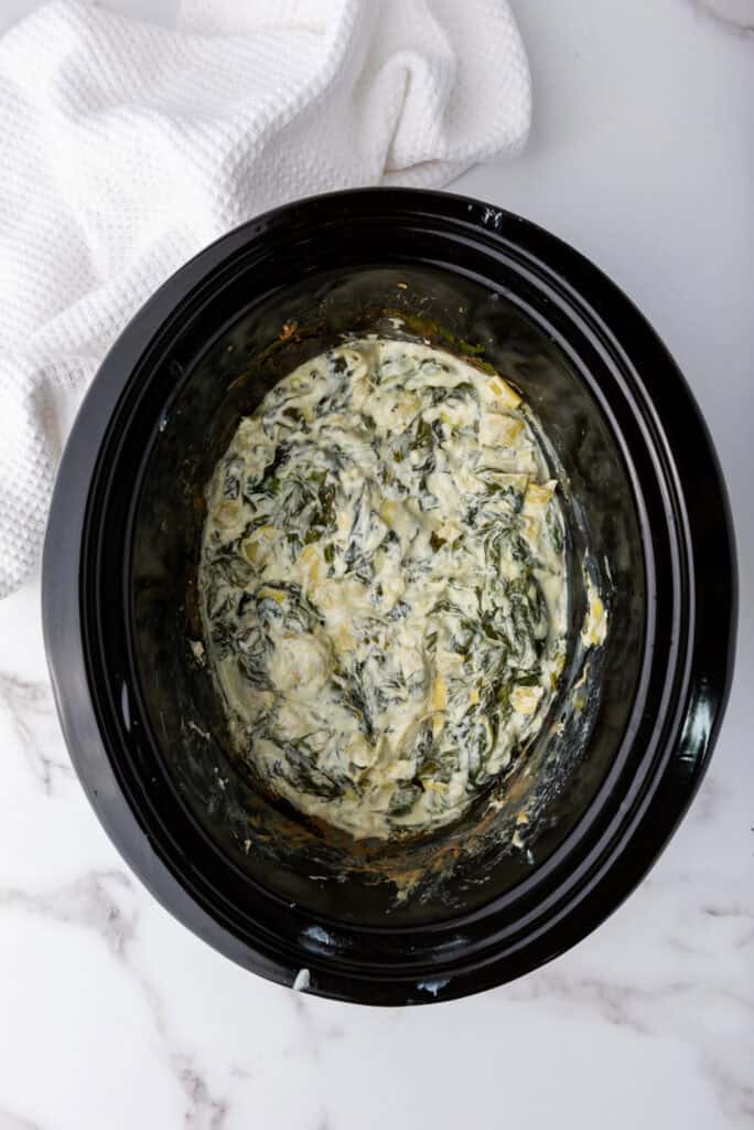 A picture of cooked spinach artichoke dip in a slow cooker.
