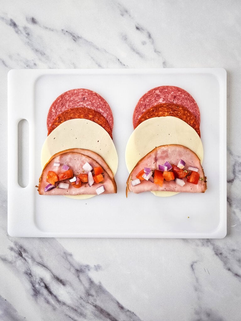 A picture of Italian meats and cheese with tomatoes, onions, and spices.