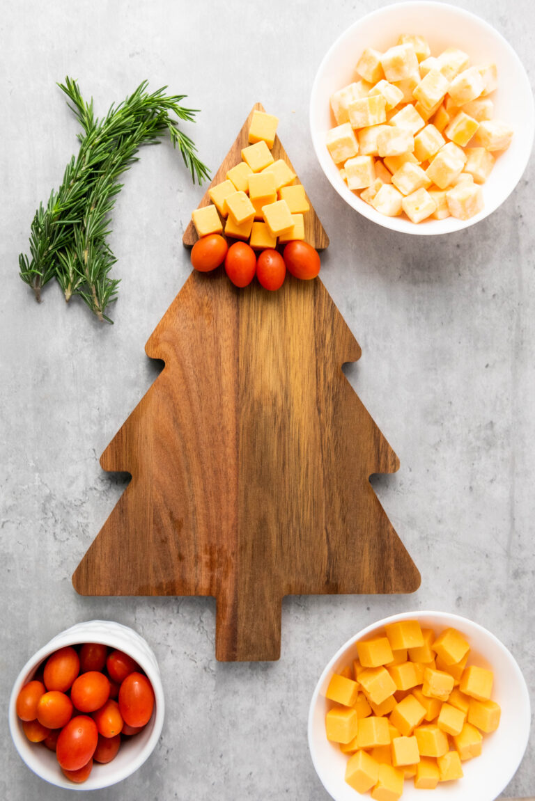 A row of cherry tomatoes layered under a row of gouda cheese forming stripes on christmas cheese board