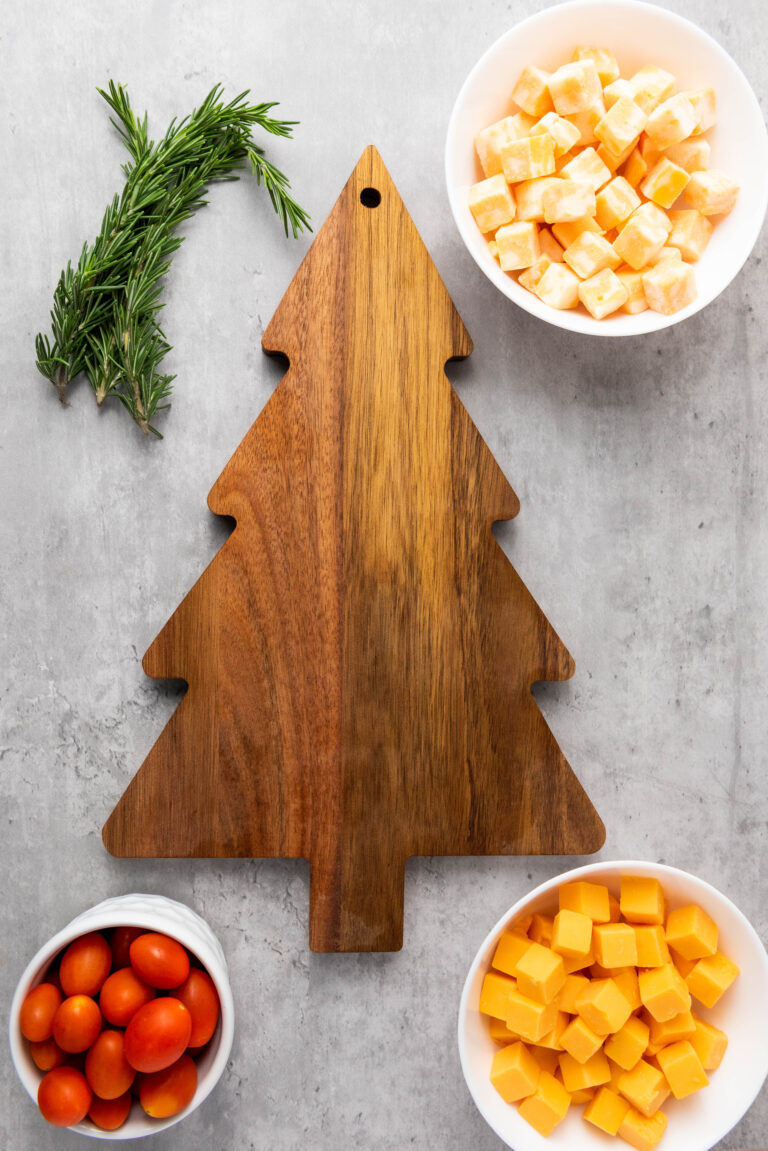DicedColby Jack and Gouda cheeses with cherry tomatoes and rosemary sprigs next to a christmas tree shaped charcuterie board.