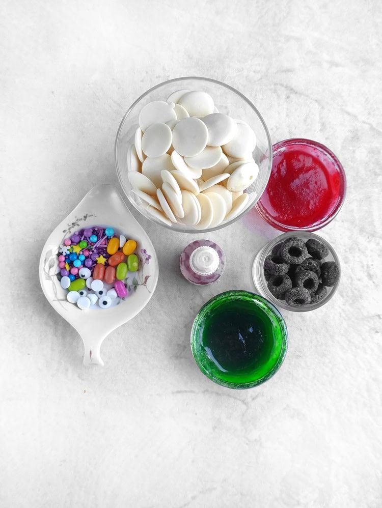 candy melts, food dye, sprinkles and other ingredients to make white chocolate halloween bark on a white table top