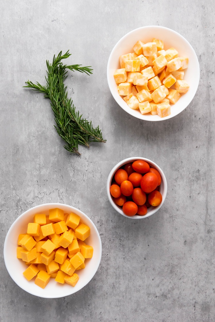 block cheeses, cherry tomatoes and herbs on a gray surface