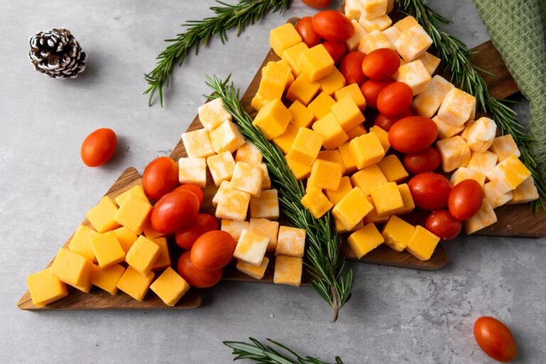 a christmas tree shaped charcuterie board with blocks of various cheeses, tomatoes and herbs