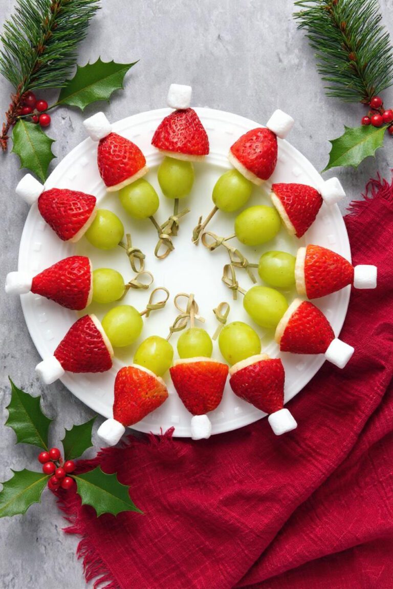 marshmallow, strabwerry, banana and grapes on skewers arranged on a table atop a red cloth with holly sprigs