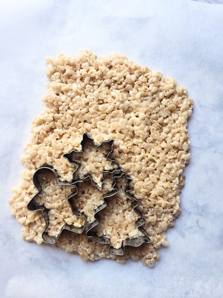 cookie cutters pressed into rice krispies mixture on a white parchment paper