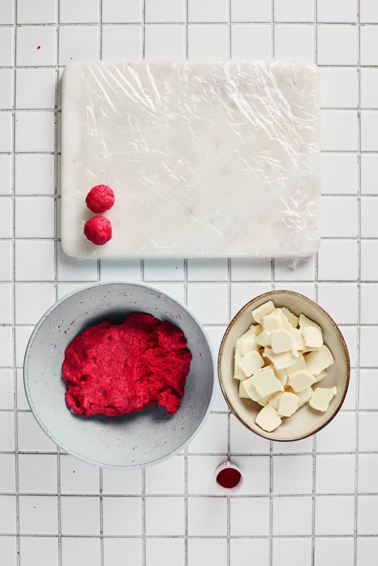A picture of two small balls of red velvet dough on a cutting board.