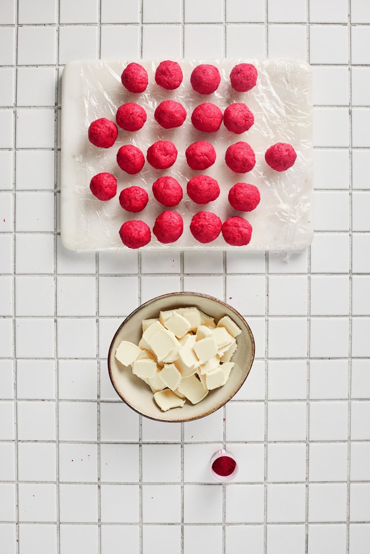 A picture of a large set of of red velvet dough balls on a cutting board.