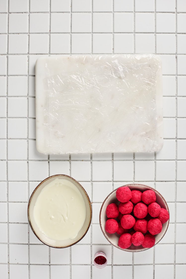 A picture of white candy melts melted in a bowl next to red velvet truffles.