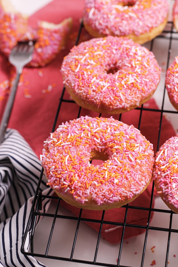 A close up picture of a donut with pink and orange sprinkles.