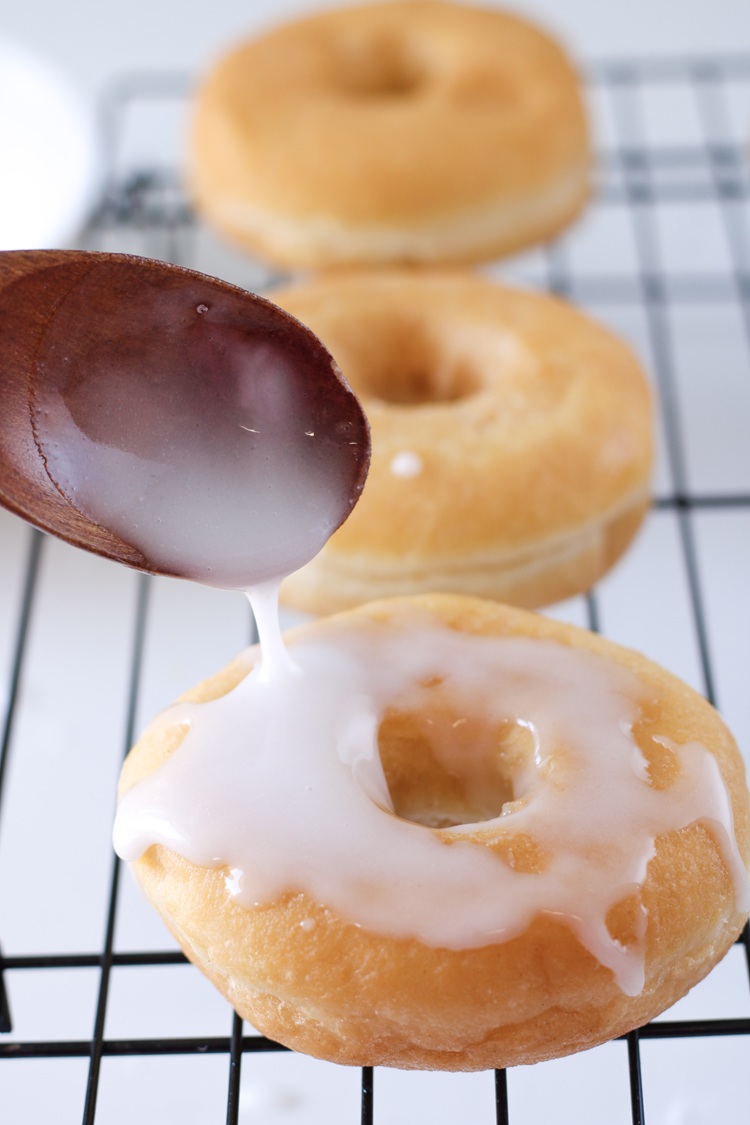 A picture of icing being poured onto a cooked donut.