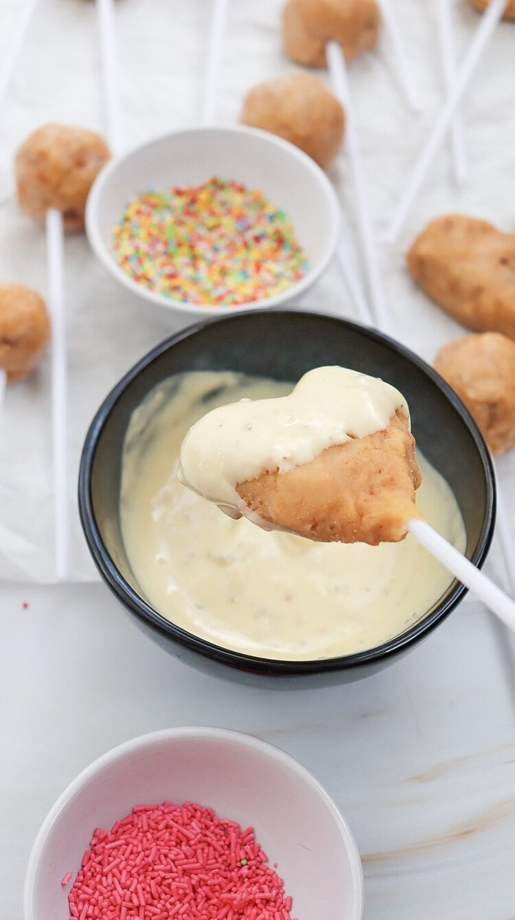 A picture of a heart shaped cake pop being coated with frosting.