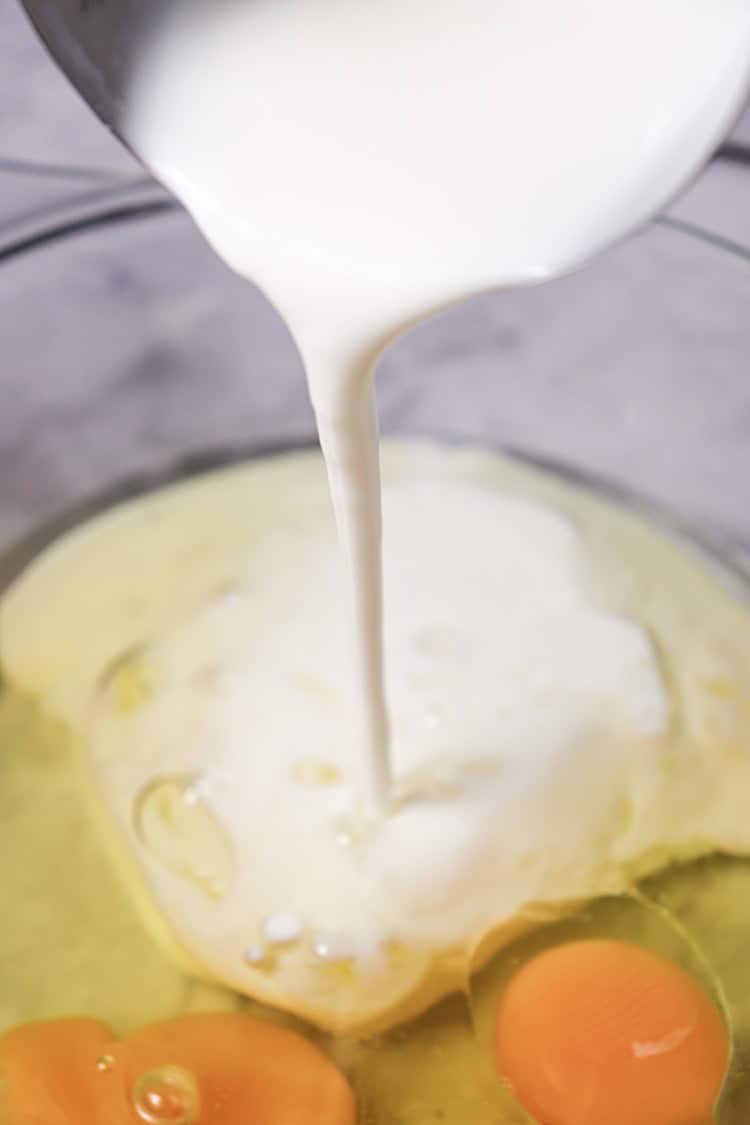 A picture of buttermilk being poured into a bowl of eggs.