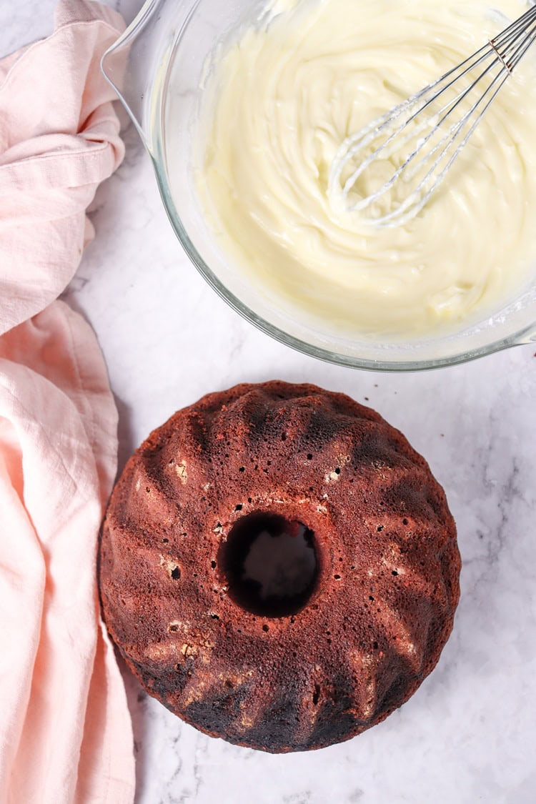 A picture of a red velvet bundt cake next to a bow of frosting.