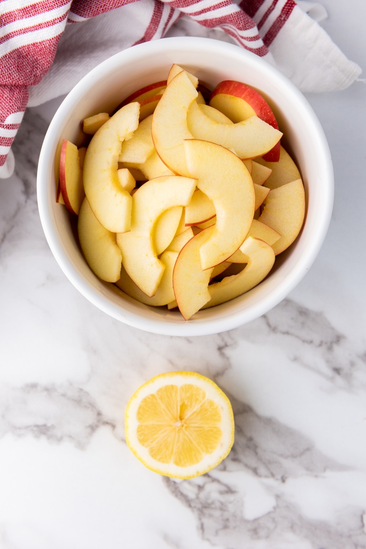 A picture of sliced apples in a bowl next to half of a lemon.