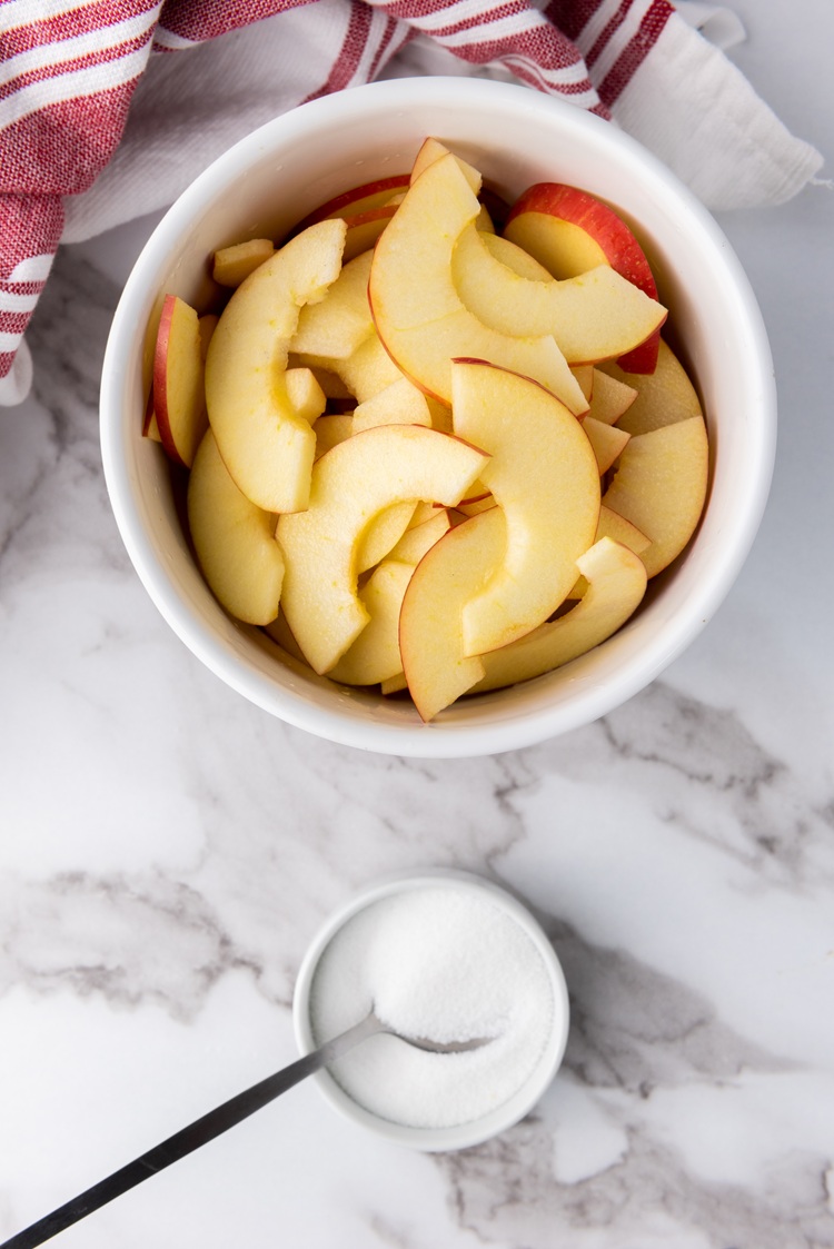 A picture of sliced apples in a bowl next to a bowl of sugar.