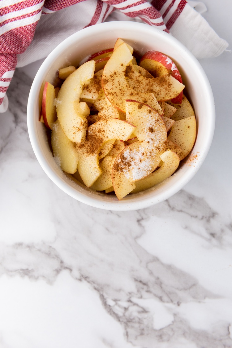 A picture of sliced apples in a bowl covered with cinnamon and sugar.