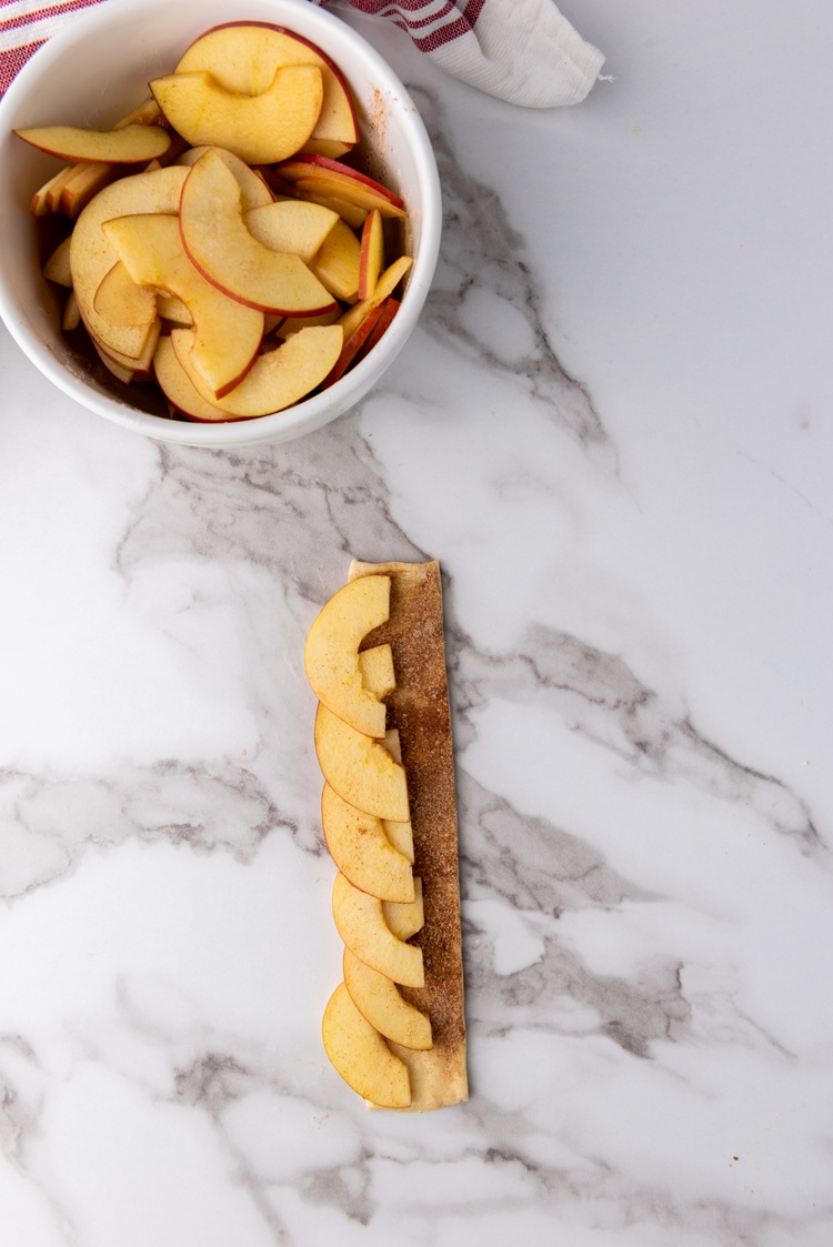 A picture of a puff pastry strip laying flat topped with apple slices.