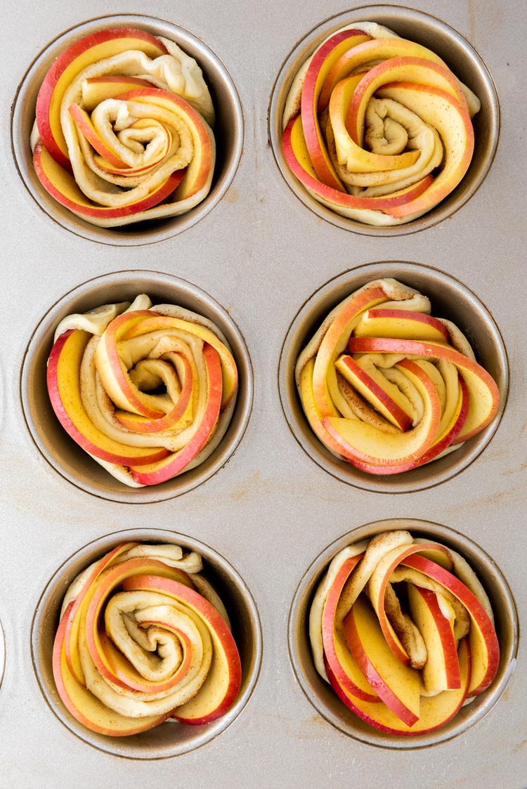 A picture of six raw puff pastry roses in a muffin tin.