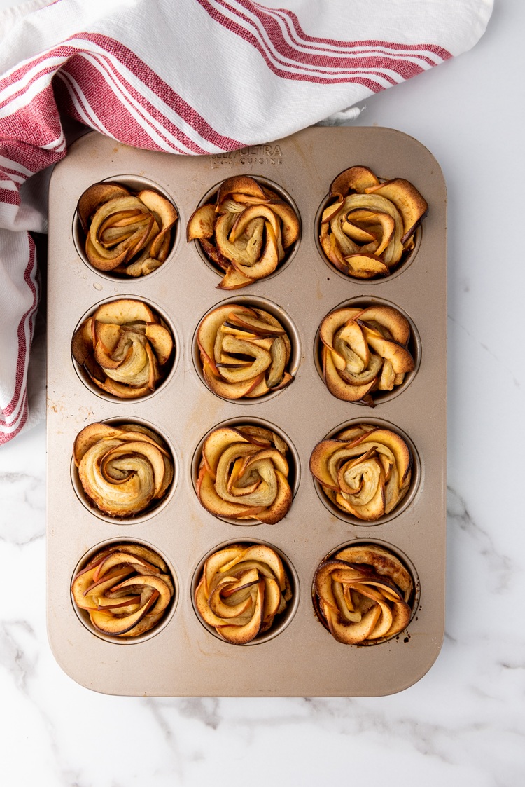 A picture of twelve baked puff pastry roses in a muffin tin.
