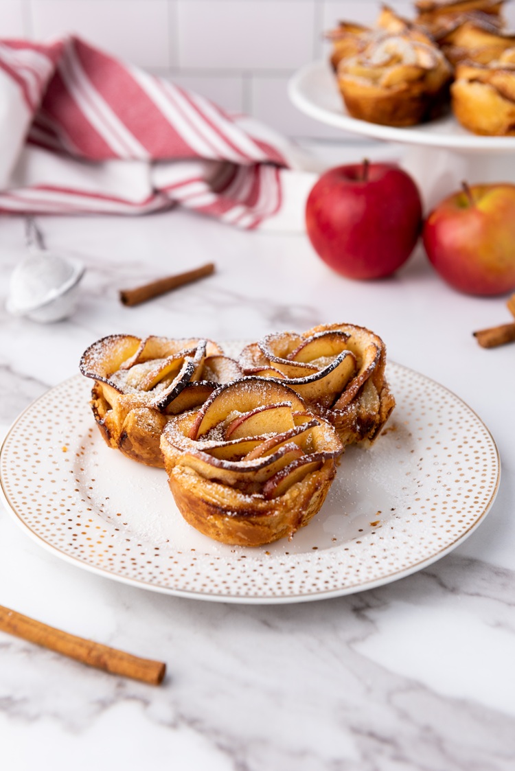A close up picture of three puff pastry apple roses on a plate.