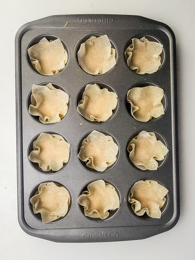 A picture of egg roll wrappers layered over shredded cheese stuffed into cupcake tins.