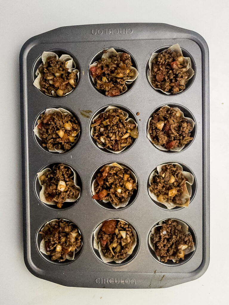 A picture of egg roll wrappers filled with a ground beef mmixture in cupcake tins.