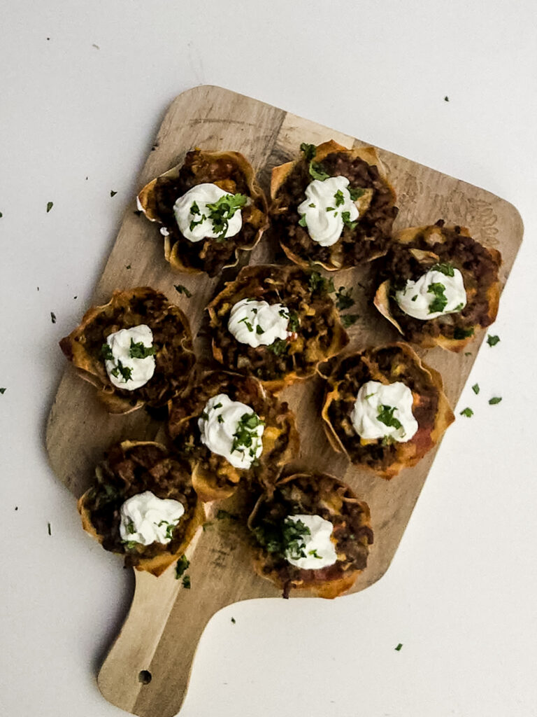 A picture of baked mini taco cups topped with sour cream and cilantro in cupcake tins.