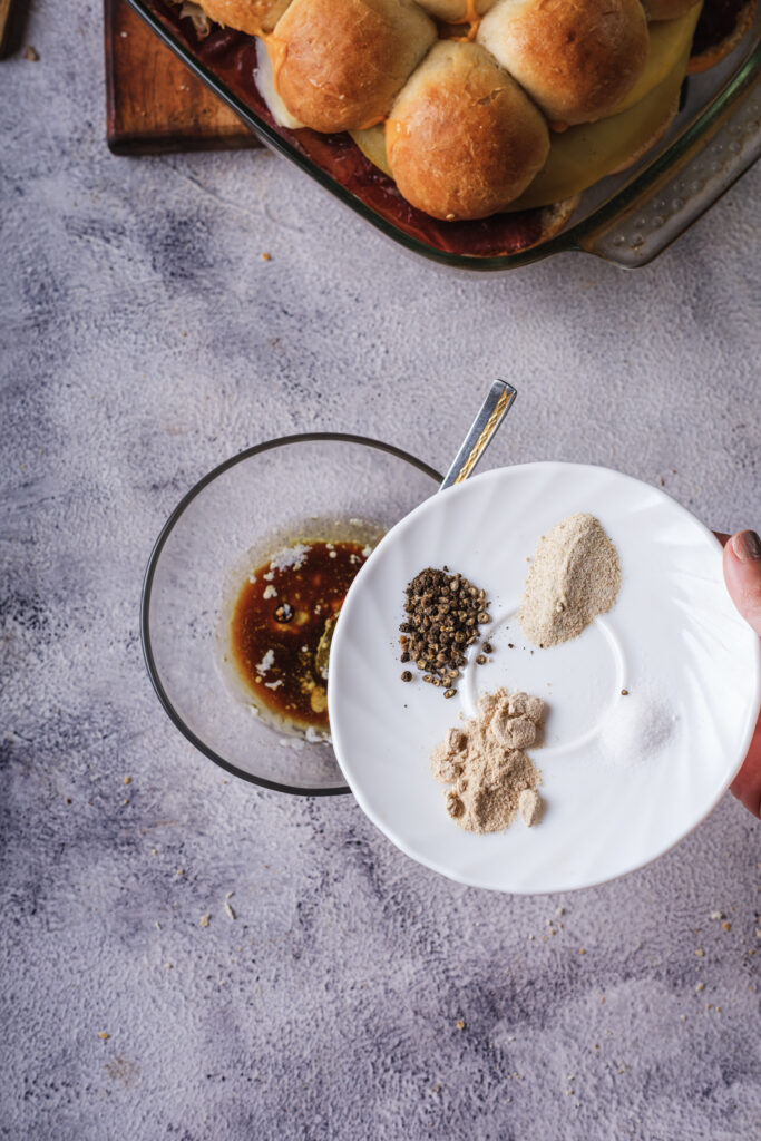 A picture of garlic powder, onion powder, Worcestershire sauce, pepper being poured into melted butter.