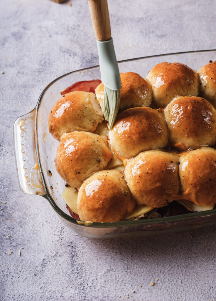 A picture of reuben sliders being brushed over the top with a garlic butter mixture.