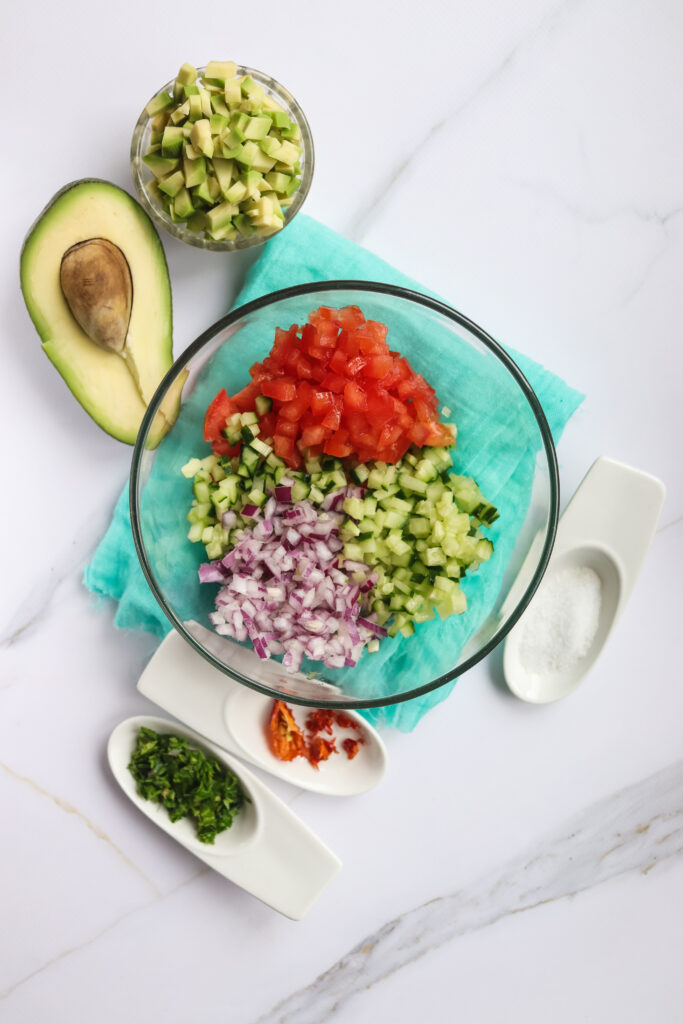 A picture of red onion, jalapeños, tomatoes, cucumber, and cilantro unmixed in a bowl.