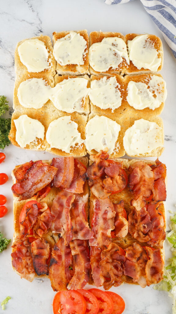 A picture of toasted sliced slider buns, topped with mayonnaise, tomato, and bacon.