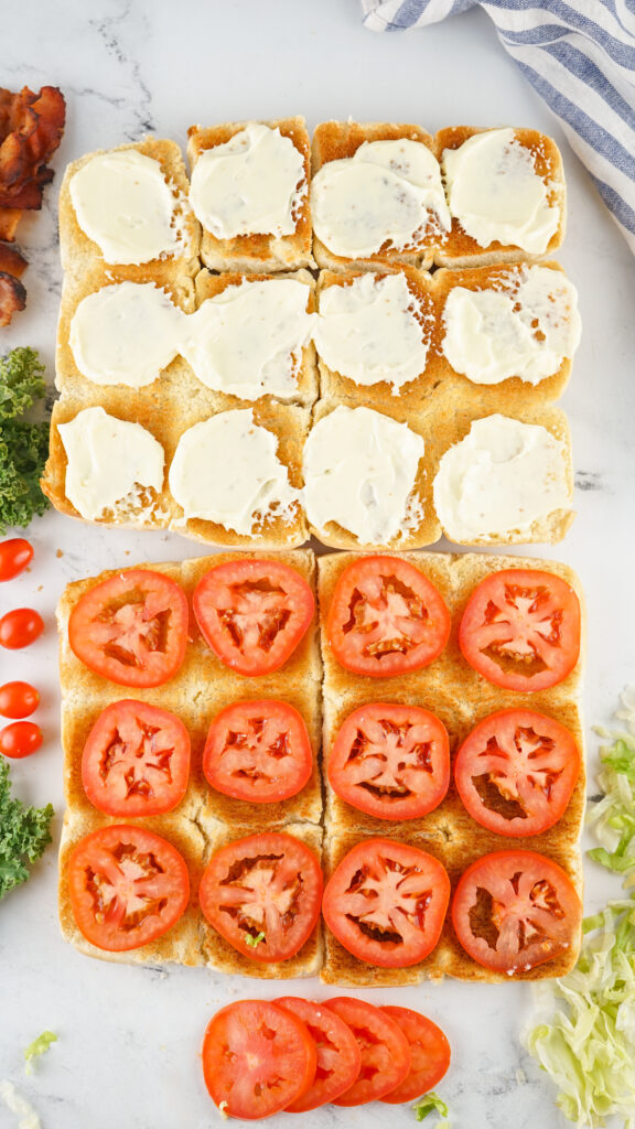 A picture of toasted sliced slider buns, with the bottom halves topped with mayonnaise and tomato.