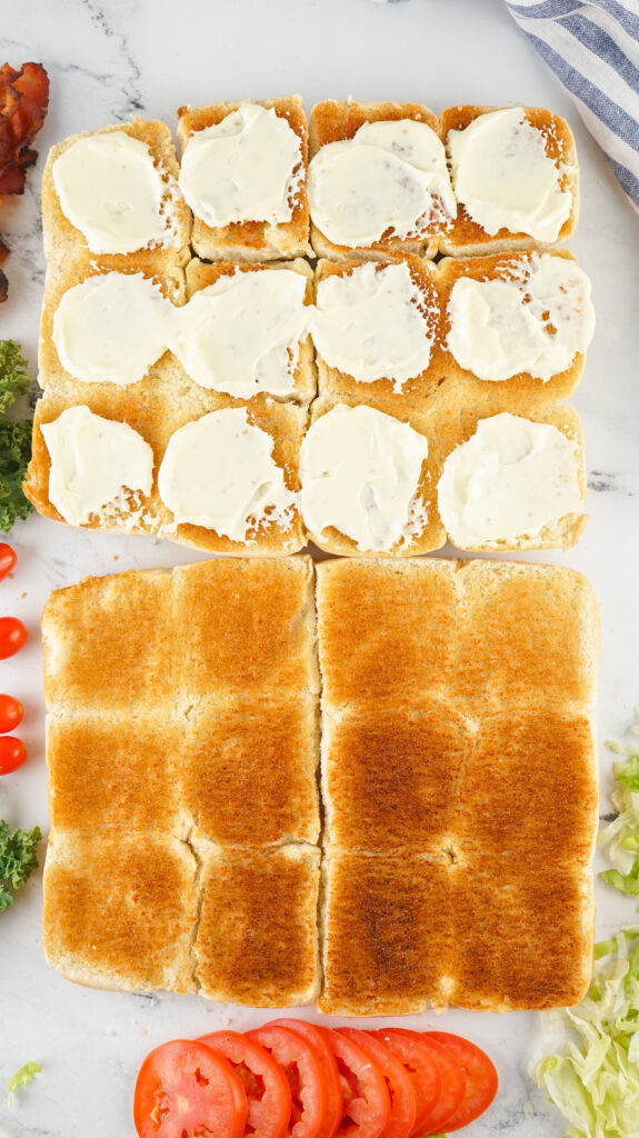A picture of toasted sliced slider buns, with the bottom halves topped with mayonnaise.