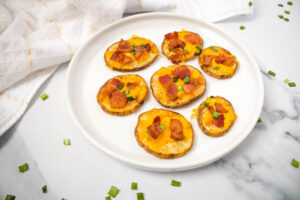 A picture of a set of bacon and cheese potato slices on a white plate.