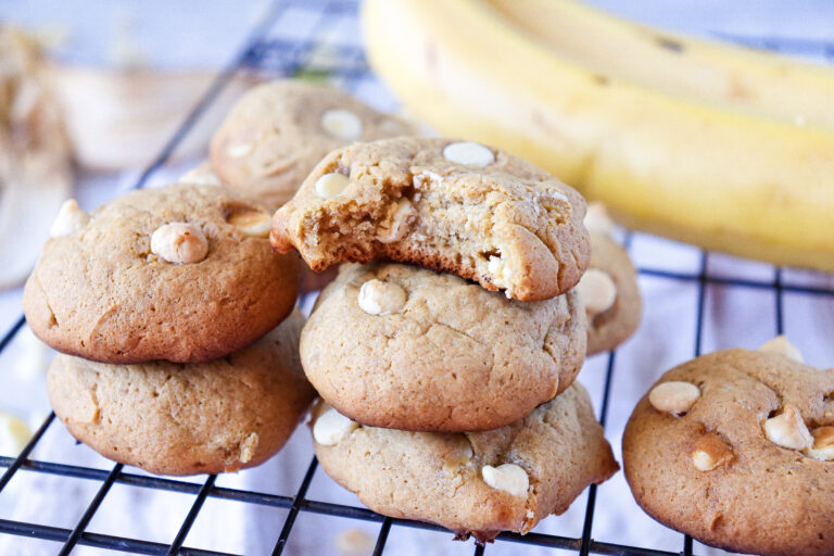 A picture of stacked banana pudding cookies on a wire rack with a bite taken out of one.